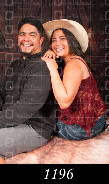 A joyful couple poses together, the woman wearing a white hat and lace top.