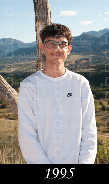 Teen boy wearing glasses and white Nike sweatshirt outdoors with mountains in background.