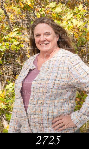 Smiling woman posing outdoors with autumn leaves in the background.