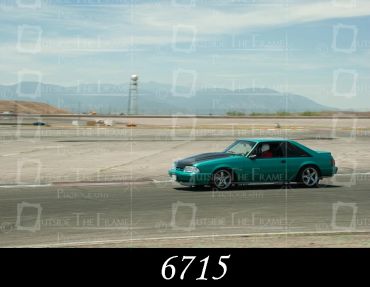 A teal sports car races on a track with mountains in the background.