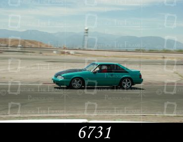 Green sports car racing on a track with mountains in the background.