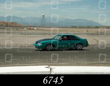A green sports car racing on a track with mountains in the background.