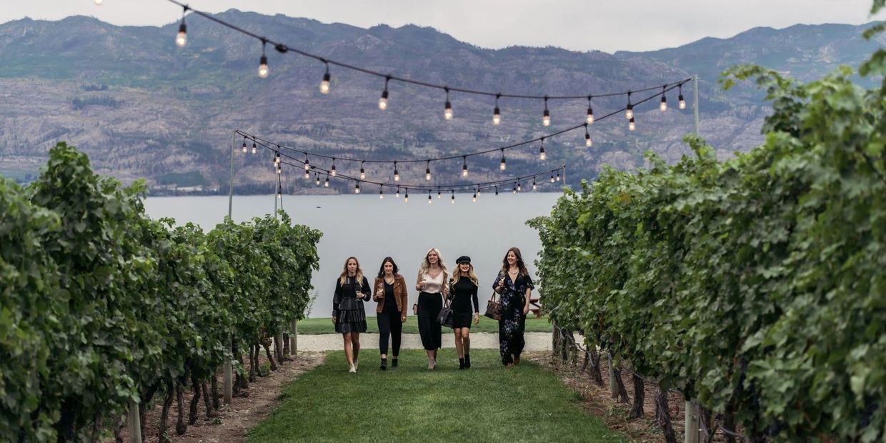 A group of smiling women walk through a lush vineyard