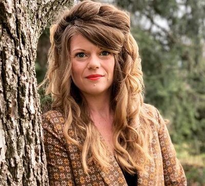Woman with styled hair leaning against a tree outdoors.