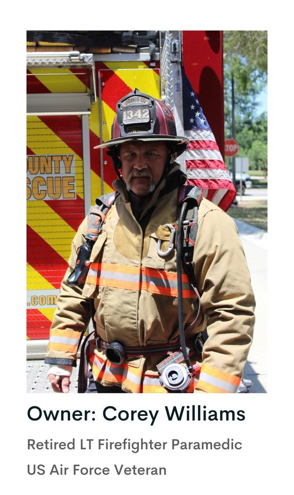 Retired firefighter in full gear standing by a rescue truck with an American flag.