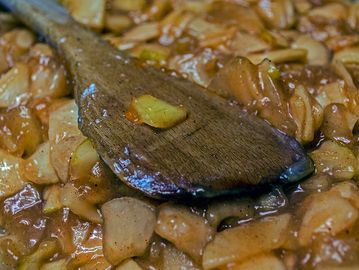 Wooden spoon stirring a thick stew with vegetables.
