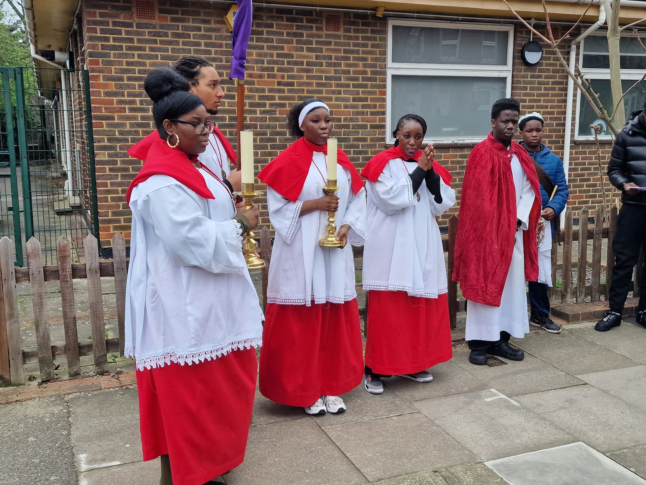 Group of young people in red and white choir robes holding candles outside.