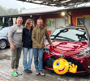 Dwóch męzczyzn i kobieta stoją przed  przodem Toyoty Yaris III w kolorze bordowym, 