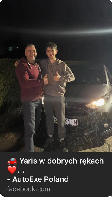 Dwóch zadowolonych mężczyzna  z kciukami w górę stoją w deszczu w nocy przed samochodem Yaris IV