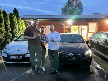 Dwóch mężczyzn i kobieta stoją uśmiechnięci przed czarnym i białym samochodem marki Renault