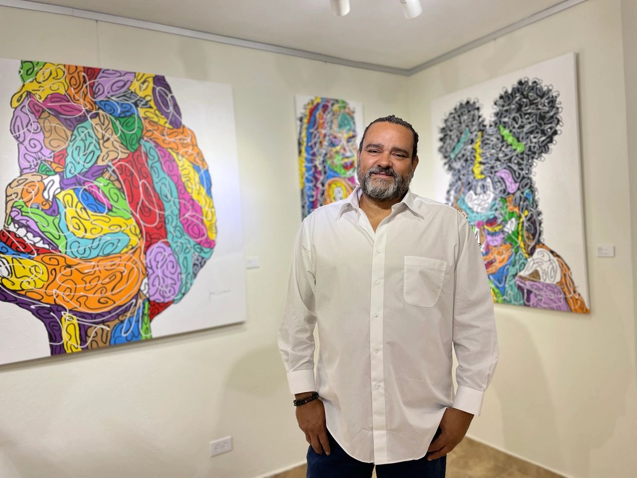Man standing in front of colorful abstract paintings in a gallery.
