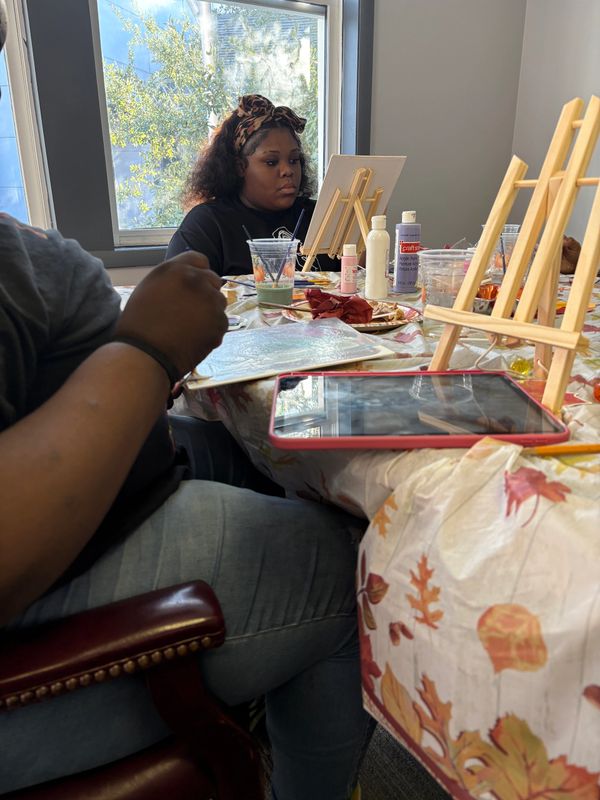 People engaged in painting at a table with autumn-themed decor.