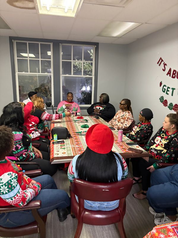 Group of people in holiday sweaters gathered around a decorated table in a room.