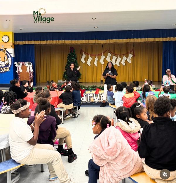 Children attending a festive event with speakers on stage and holiday decorations.