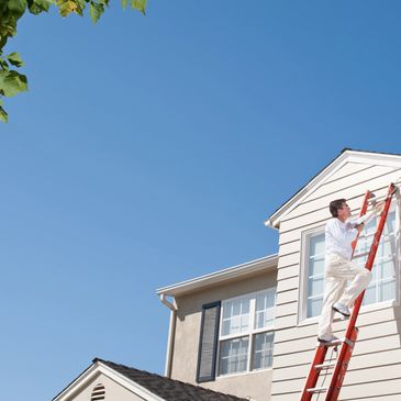 man on a ladder painting exterior of a house