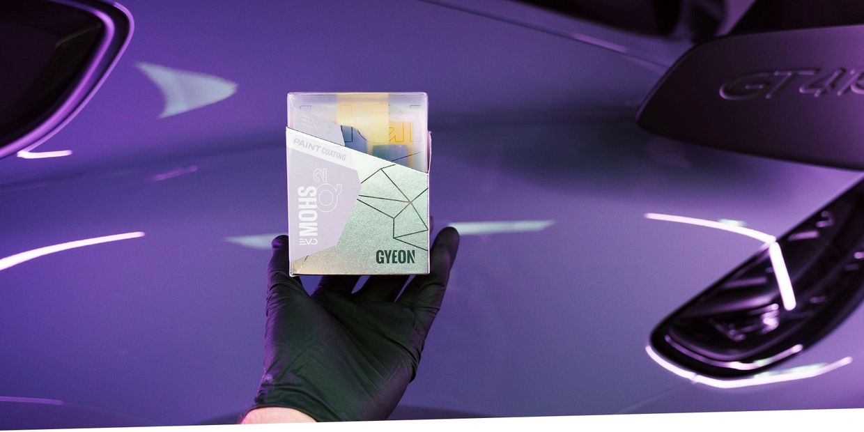 Hand holding Gyeon Mohs2 paint coating box in front of a shiny car.