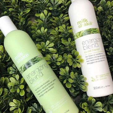 Two Milk Shake hair care bottles on green leaves background.