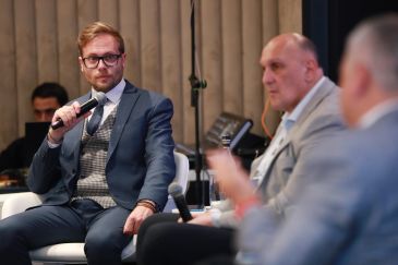 Man in suit holding a microphone at a panel discussion.