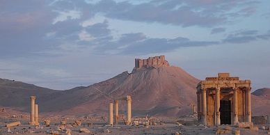 Ancient ruins with a desert mountain backdrop under a cloudy sky.