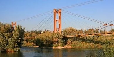 A suspension bridge over a river surrounded by greenery under a clear sky.