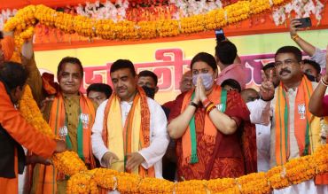 A group of political leaders at a public event decorated with orange marigold garlands.