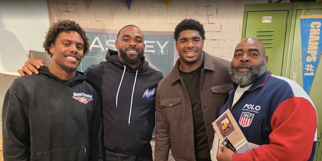 Four men smiling together in a casual indoor setting with colorful decor.