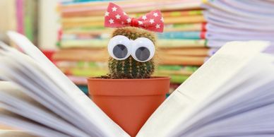A cactus with googly eyes reading a book.