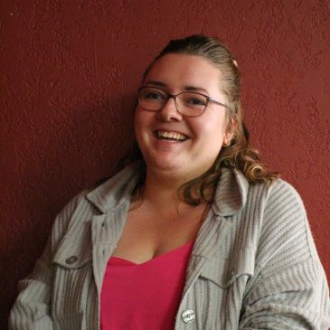 Smiling woman with glasses against a red wall.