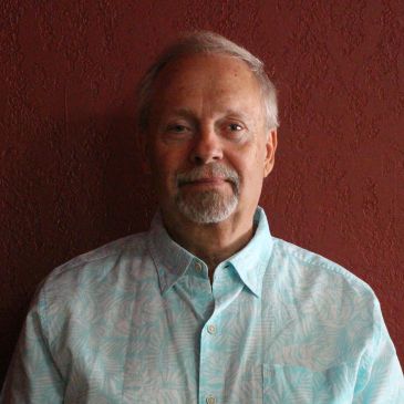 Older man with short gray hair and beard, wearing a light blue patterned shirt.