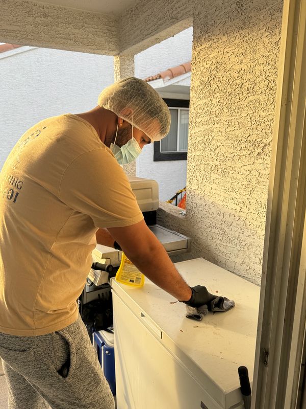 Persona limpiando una superficie externa con guantes y mascarilla.