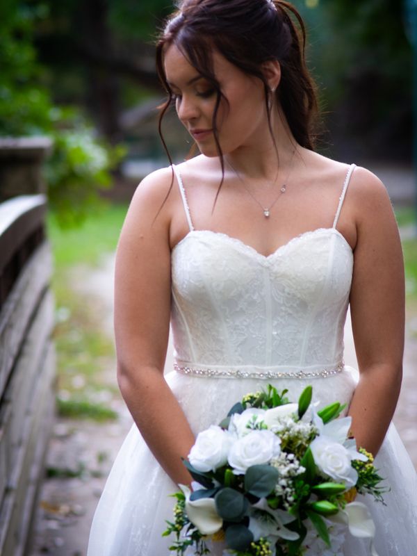 Bride in a white lace wedding dress holding a bouquet of white flowers outdoors.