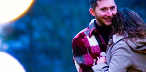 Couple sharing a warm embrace outdoors at dusk.