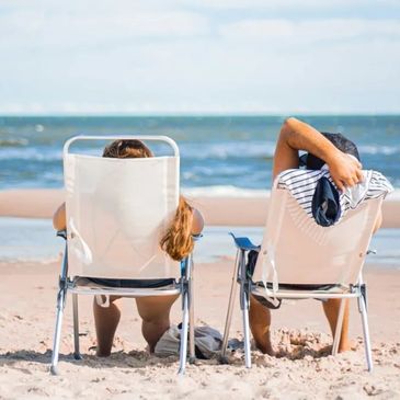 Two people relaxing on beach chairs facing the ocean.