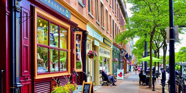 Colorful storefronts and outdoor seating line a lively, tree-lined street.