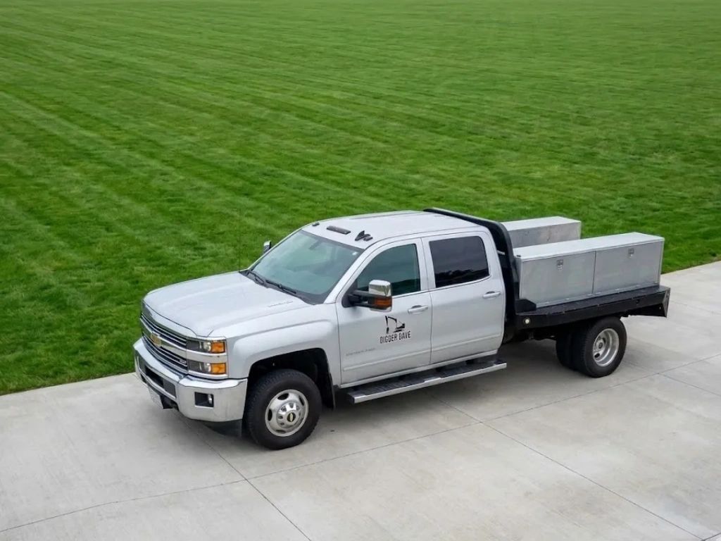 White pickup truck with a flatbed and storage boxes on a driveway.