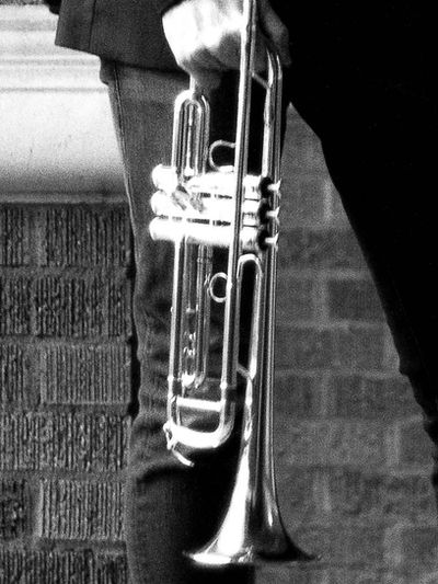 Close-up of a person holding a trumpet against a brick background.