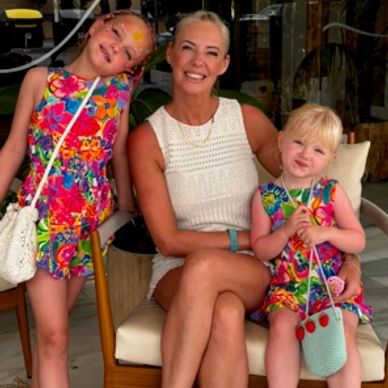 Mother with two daughters in colorful dresses smiling.