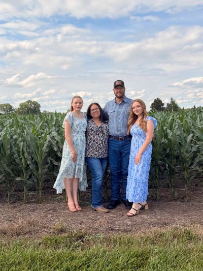 Family of four posing in front of a cornfield.