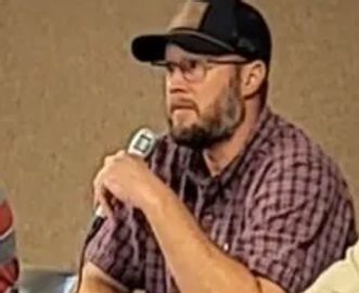 Man in plaid shirt holding a microphone.