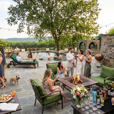 Guests enjoy drinks and conversation around a firepit by a pool.
