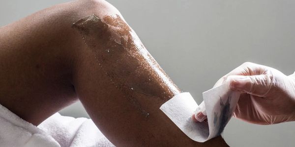 A person removing wax strips from their leg for hair removal.