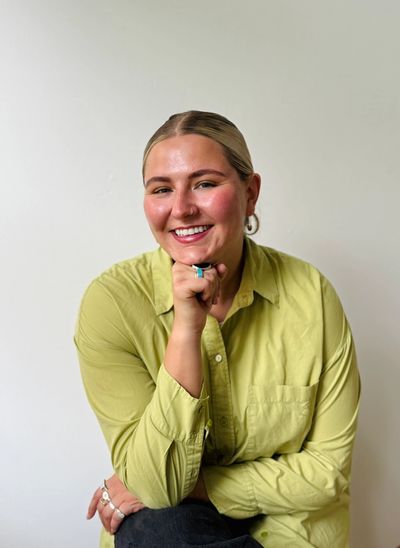 A smiling woman in a light green shirt posing against a white wall.