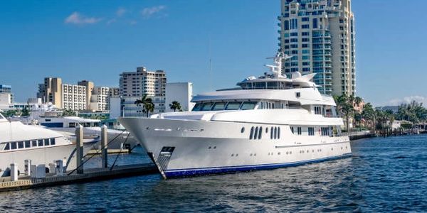 Luxurious white yacht docked in a marina near city buildings on a clear day.