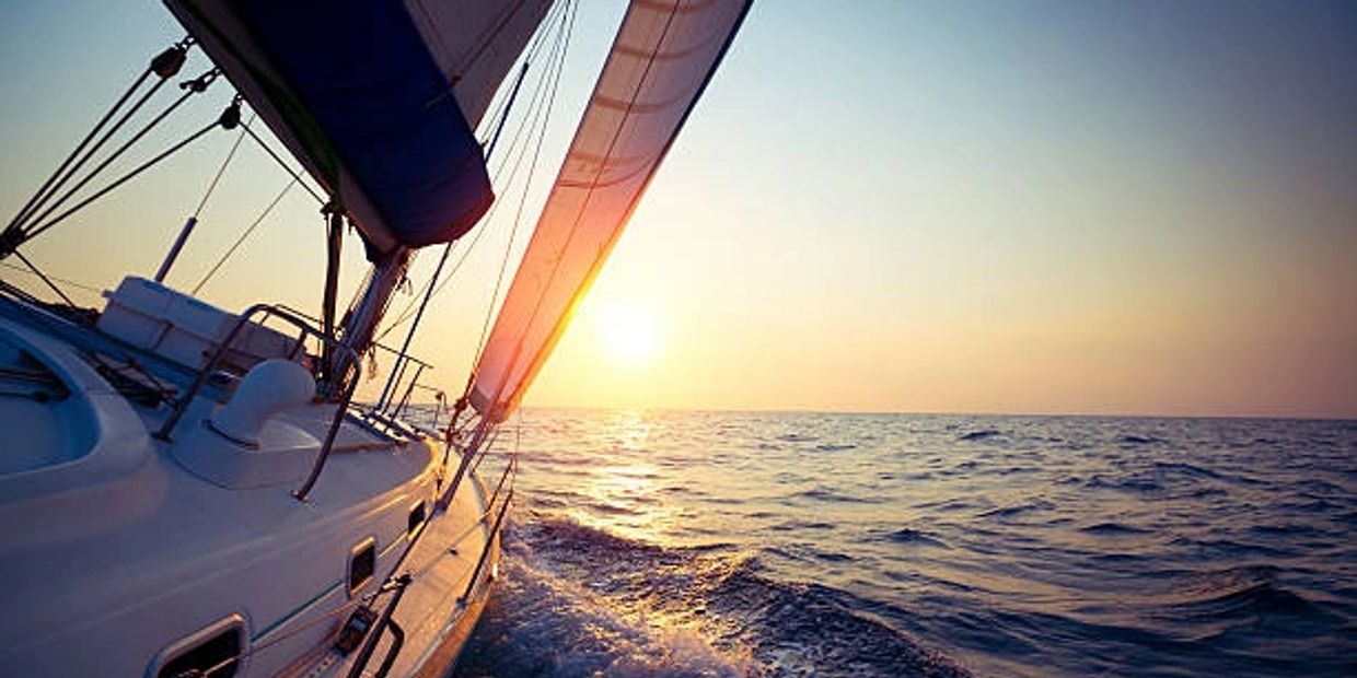 Sailboat gliding on the ocean at sunset with vibrant sky colors.