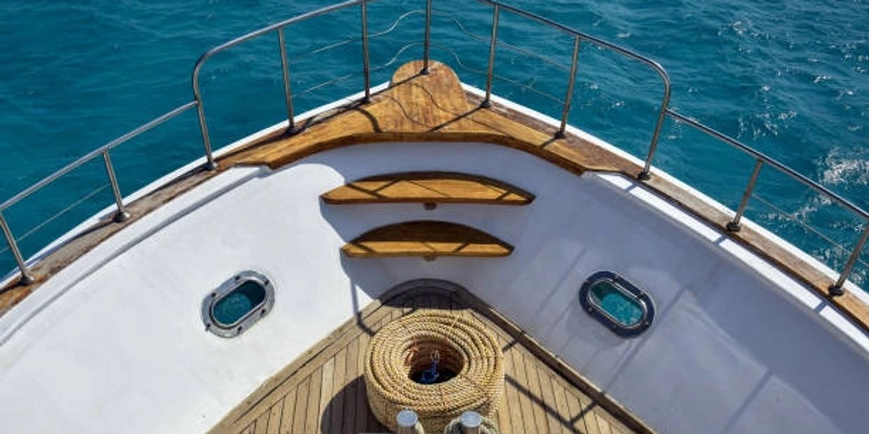 View of a boat's bow with coiled rope and blue ocean water.