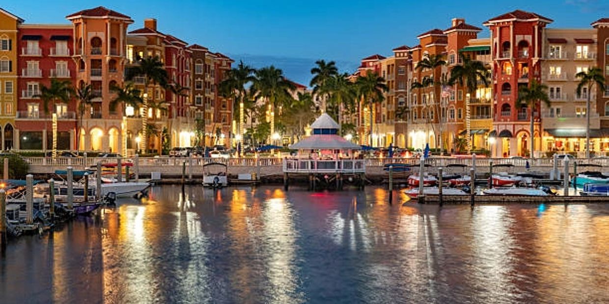 Evening view of a waterfront marina with colorful buildings and palm trees.