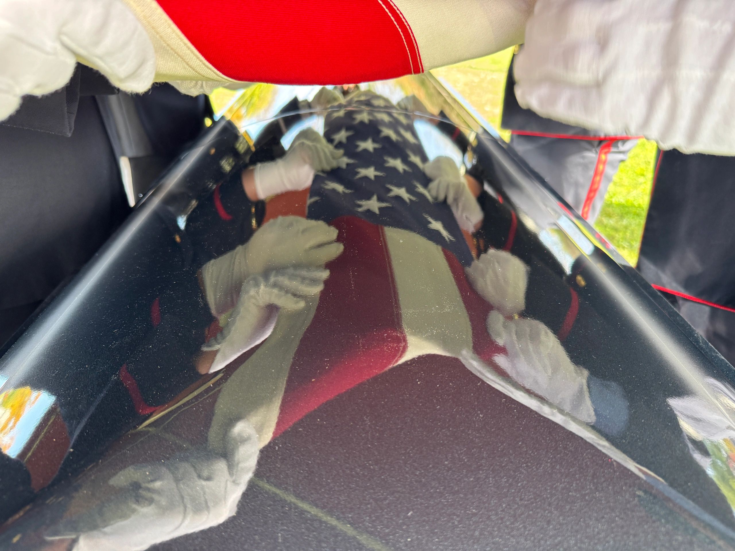 Reflection of military personnel folding an American flag over a casket.