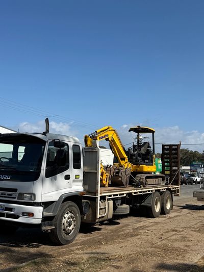 A white truck carrying a yellow Komatsu excavator.