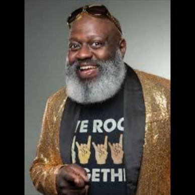 Smiling man with a gray beard wearing a gold jacket and rock-themed T-shirt.