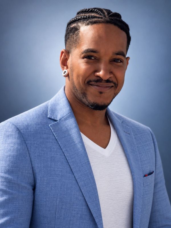 Man with braided hair wearing a blue blazer and white shirt.